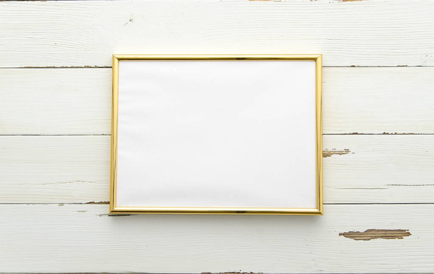 Golden photo frame for painting or picture on white wooden background. Flat lay, top view. Horisontal mockup - Photo, Image