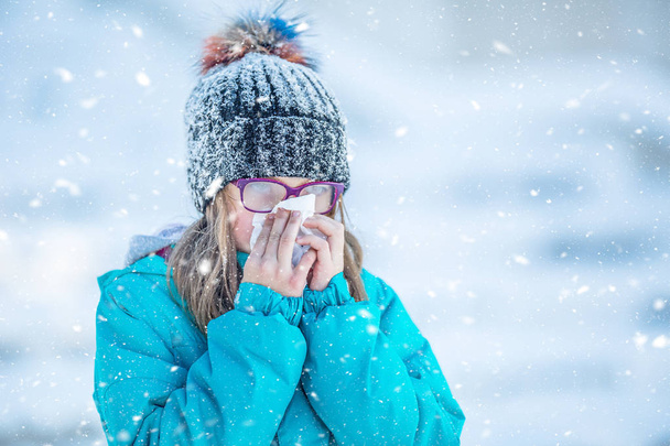 Girl with allergy symptom blowing nose. Teen girl using a tissue in a winter park - Foto, Imagem