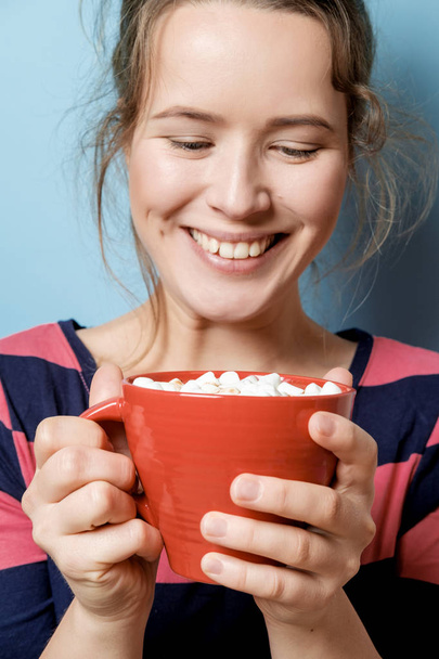 Pretty young woman with red mug against blue  background. Studio - 写真・画像