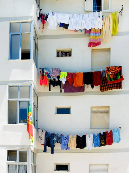 White block of apartments with of colourful washing hanging from 3 seperate floors, the washing is red, yellow, green, blue etc. - Photo, Image