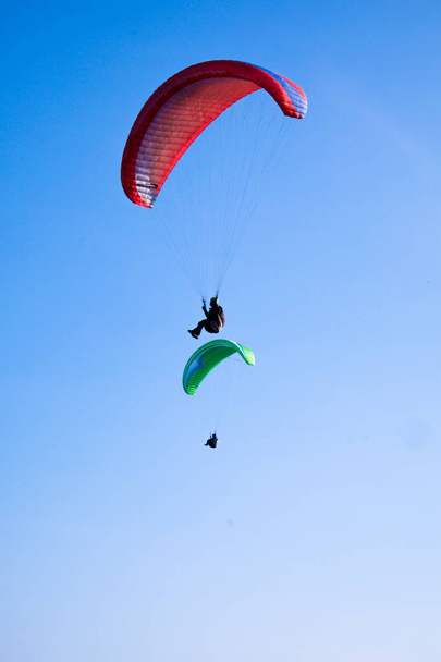 2 Gleitschirme fliegen im klaren blauen Himmel, 1 roter und 1 grüner Fallschirm. - Foto, Bild
