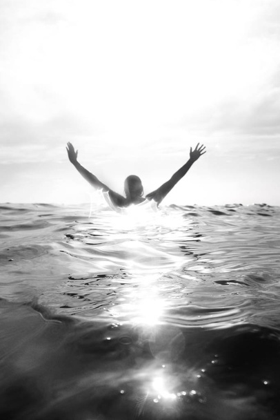 Γυναίκα 52 ετών παλιά στέκεται σε μια ήρεμη θάλασσα, πλάτη και τα χέρια είναι έξω από το νερό, κρατά τα χέρια της πάνω από το κεφάλι - Φωτογραφία, εικόνα