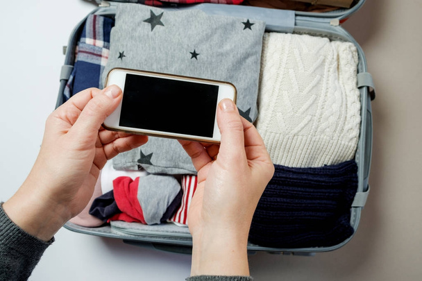 Woman hands with phone on the background of Open suitcase packed - Φωτογραφία, εικόνα