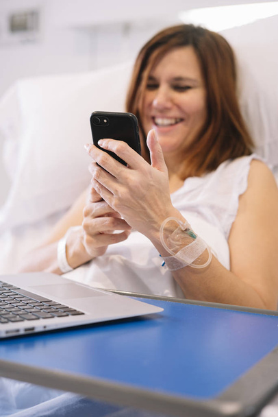 Kranke Frau mit Smartphone und Laptop im Krankenhaus - Foto, Bild