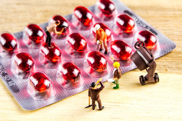 trabalho em equipe de estatuetas em miniatura com um monte de pílulas vermelhas
 - Foto, Imagem