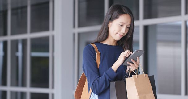 Mulher usando telefone celular e sacos de compras
 - Foto, Imagem