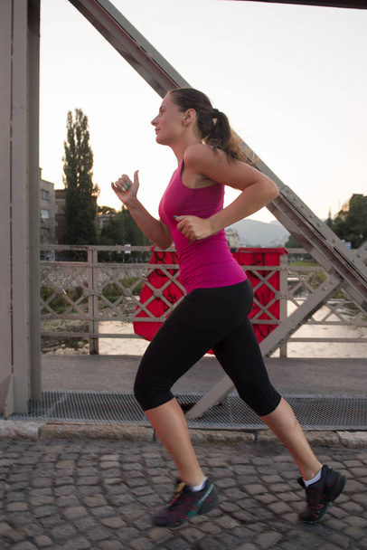 woman jogging across the bridge at sunny morning - Foto, afbeelding
