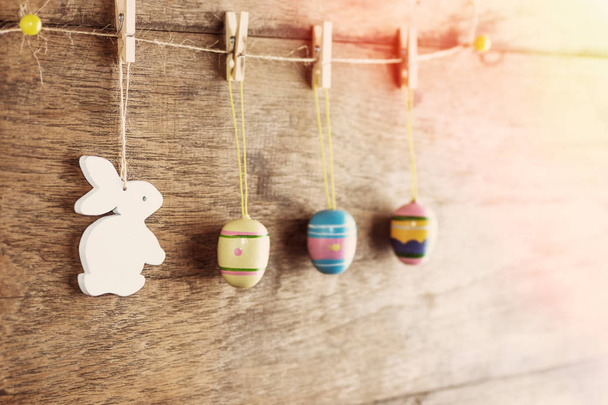 Rustieke Pasen achtergrond: Vintage beschilderde eieren en witte konijntje hang op wasknijpers tegen oud bruin houten muur. Concept van de vakantie. Tekst ruimte - Foto, afbeelding