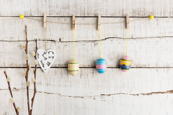 Fondo rustico pasquale: uova dipinte vintage e cuore bianco appesi a mollette contro la vecchia parete di legno bianco. Concetto vacanza. Spazio di testo
 - Foto, immagini