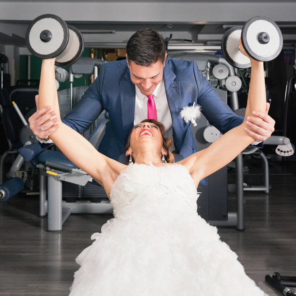 Bräutigam hilft Braut mit Gewichten im Fitnessstudio - Foto, Bild