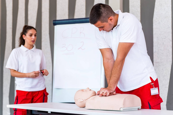 CPR-Kurs mit Instruktoren, die Erste Hilfe, Kompressionen und Reanimation mit CPR-Attrappe auf dem Tisch vorführen - Foto, Bild