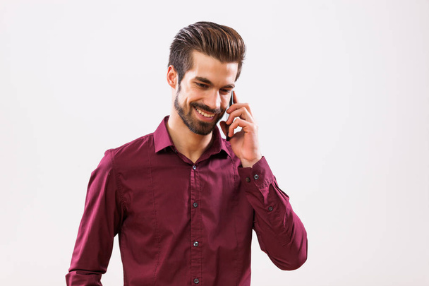 Studio shot portrait of young businessman who is talking on phone.  - 写真・画像