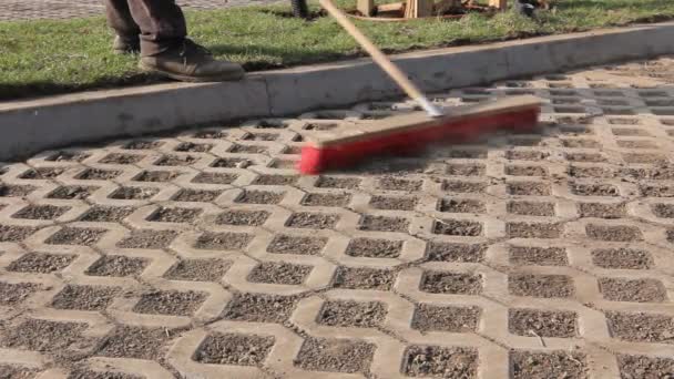 Pracovník je čištění moderní dlážděné s červeným koště, které pracovník zametá suché špíny s široké koště, čištění pomocí kartáčku zpevněné městský prostor. - Záběry, video