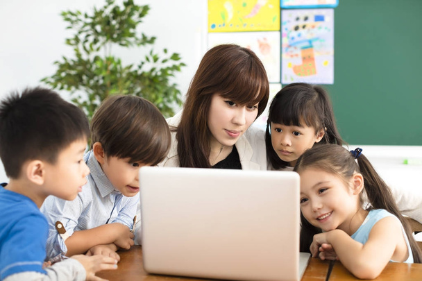 kinderen kijken op de laptop met leraar in de buurt van door - Foto, afbeelding