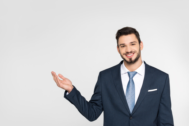 handsome young businessman showing copy space and smiling at camera isolated on grey - Φωτογραφία, εικόνα