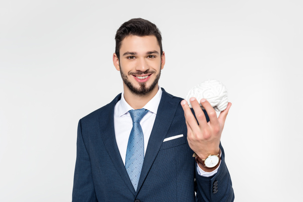 young businessman holding brain model and smiling at camera isolated on grey - Foto, Bild
