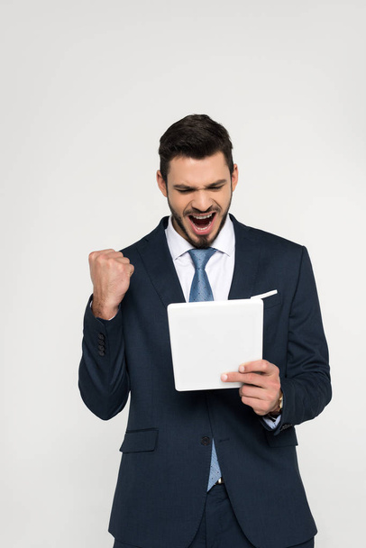 triumphing young businessman holding digital tablet isolated on grey - Fotoğraf, Görsel