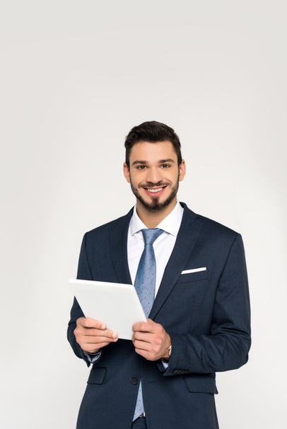 handsome young businessman holding digital tablet and smiling at camera isolated on grey - Photo, Image