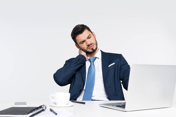 young businessman with closed eyes suffering from pain in neck while using laptop at workplace    - Foto, Imagen