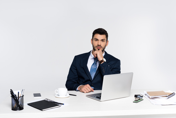 handsome young businessman using laptop and looking at camera at workplace - Foto, imagen
