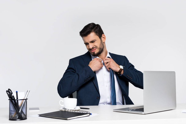 giovane uomo d'affari oberato di lavoro regolazione cravatta mentre seduto sul posto di lavoro
  - Foto, immagini