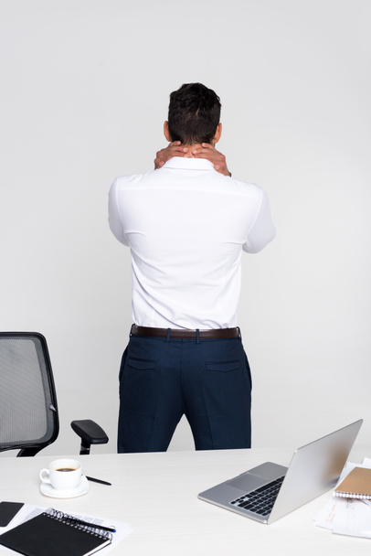 back view of young businessman suffering from pain in neck while standing at workplace - Фото, зображення
