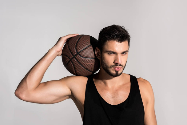 handsome young basketball player with ball isolated on grey - Foto, imagen