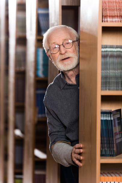 bibliotecario pelo gris feliz mirando desde el estante
  - Foto, Imagen