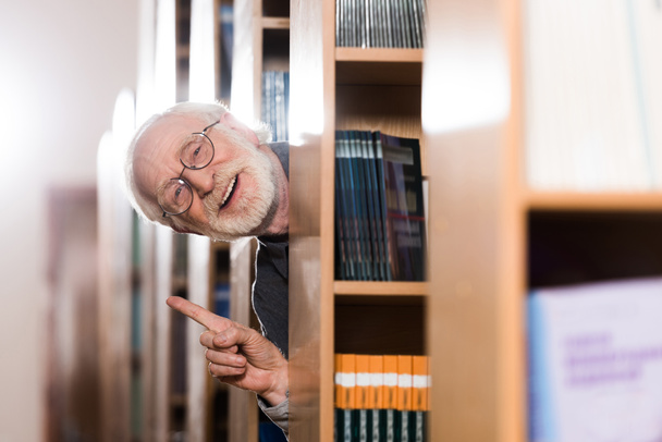 bibliothécaire cheveux gris heureux regardant hors de l'étagère et montrant geste idée
  - Photo, image