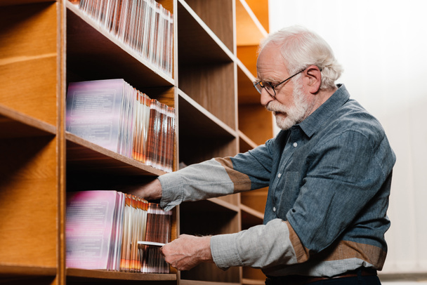 side view of grey hair librarian searching for book - Foto, Bild
