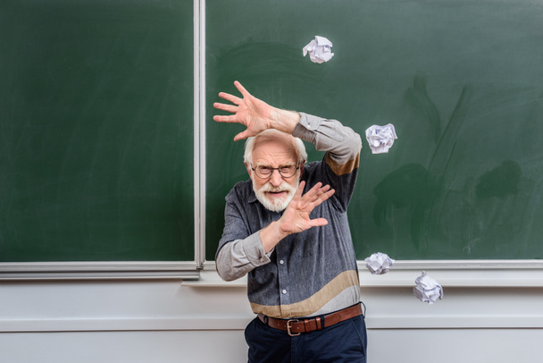 profesor senior protegiéndose de caer pedazos arrugados de papel
  - Foto, imagen
