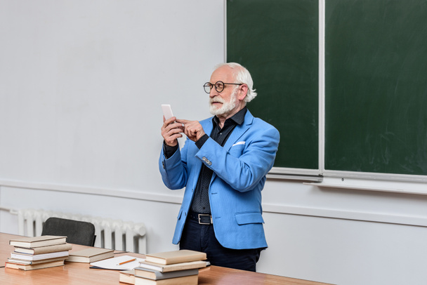 grey hair professor looking at smartphone in lecture room - Fotó, kép