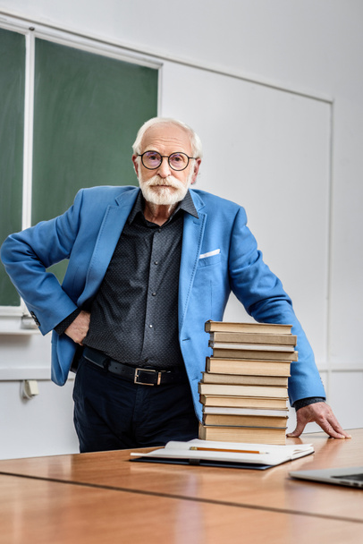 професор сірого волосся стоїть біля стопки книг
 - Фото, зображення