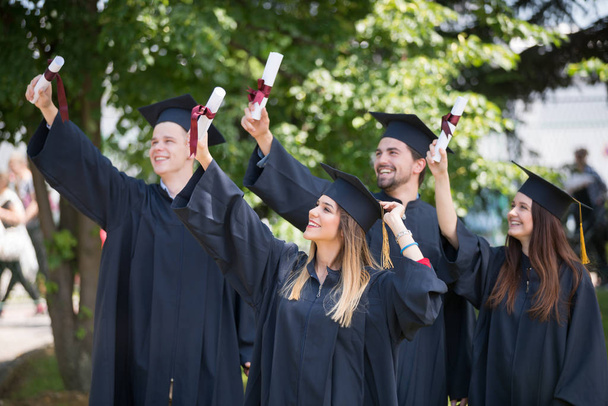 education, graduation and people concept - group of happy international students in mortar boards and bachelor gowns with diplomas - Zdjęcie, obraz