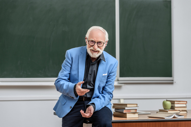 smiling grey hair professor sitting on table in lecture room - Foto, Imagem