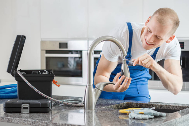 Happy plumber repairing kitchen's faucet - Fotografie, Obrázek