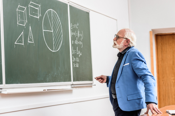 grey hair professor holding piece of chalk and looking at blackboard - Photo, Image