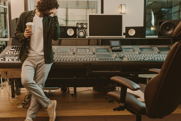 νέος παραγωγός ήχου στέκεται στο studio με φλιτζάνι καφέ να πάει - Φωτογραφία, εικόνα