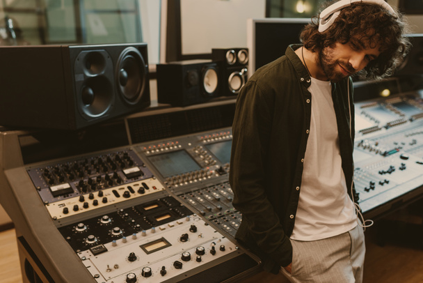 sound producer in headphones leaning back on recording equipment at studio - Fotografie, Obrázek