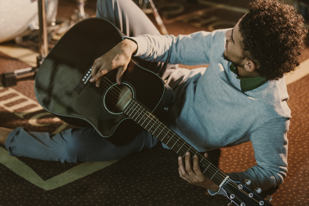 hombre afroamericano guapo acostado en el suelo del estudio con guitarra acústica
 - Foto, imagen