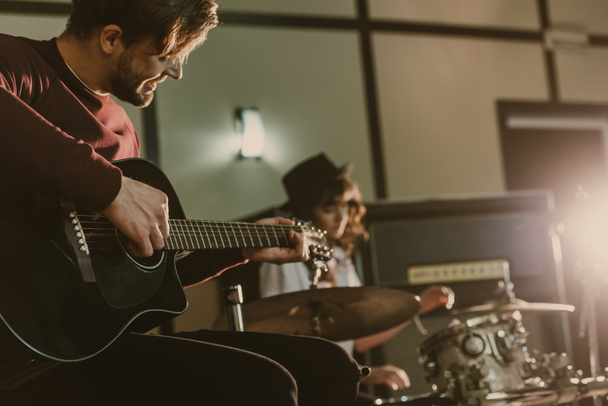 handsome young musician playing guitar on repetition with blurred female drummer behind - 写真・画像