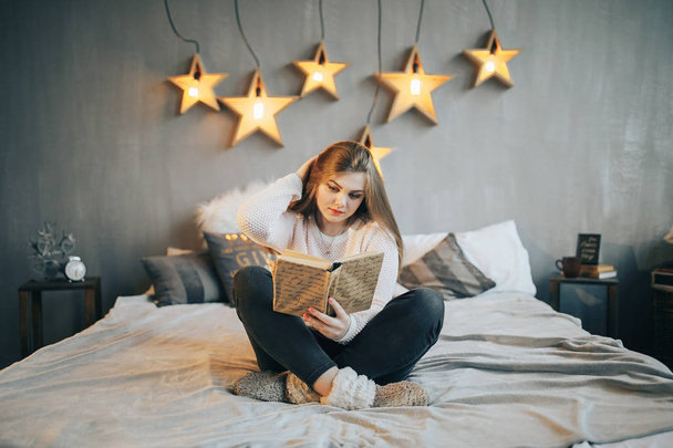 Lány az ágyban, egy könyvet olvas fekvő hasán mosolygós boldog - Fotó, kép