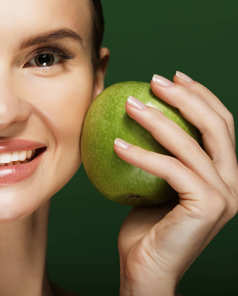 Head shot of woman holding green apple against green background - Foto, immagini