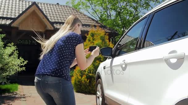 Slow motion footage of young female driver making photos on smartphone of her car for sell - Séquence, vidéo