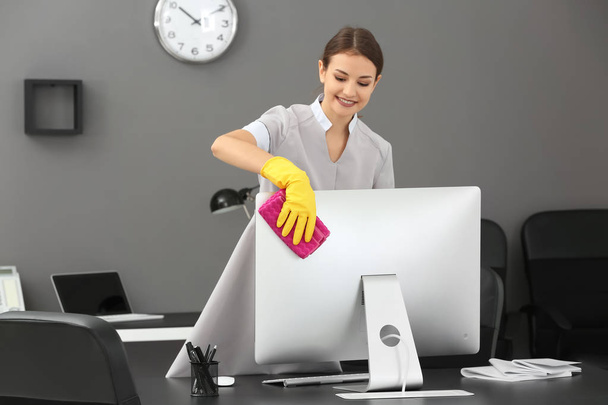 Young woman removing dust in office - Foto, imagen