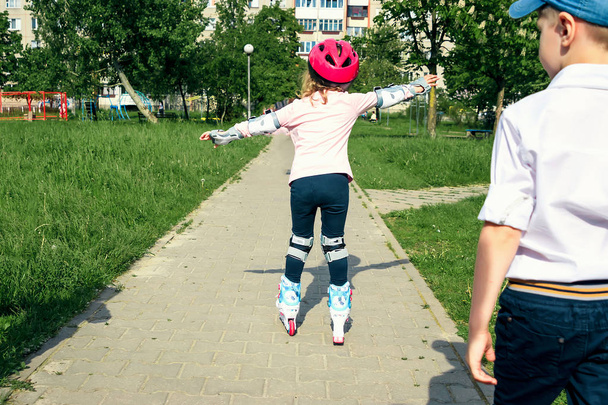The girl learns to skate on the street. Children wear protective pads and a protective helmet for safe riding on rollers. Active sports activities for children - Foto, immagini