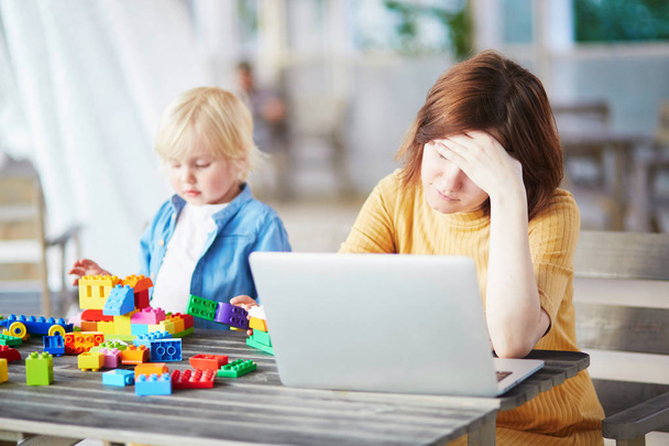 Little boy playing with construction blocks while his mother working on computer - Фото, изображение