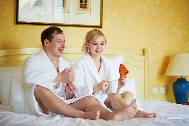 Couple in white bathrobes in bed, drinking coffee - Zdjęcie, obraz