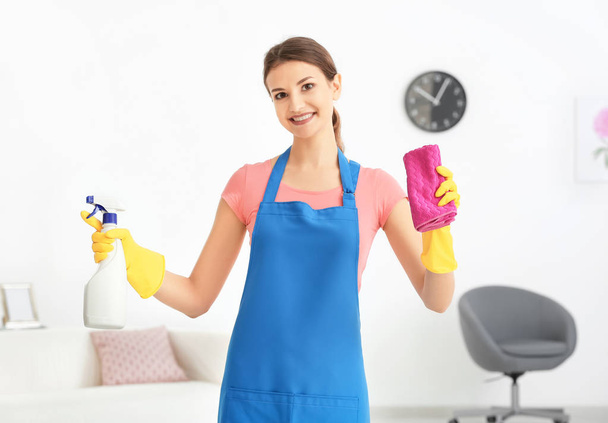 Young woman with bottle of detergent and rag in flat - Foto, Bild