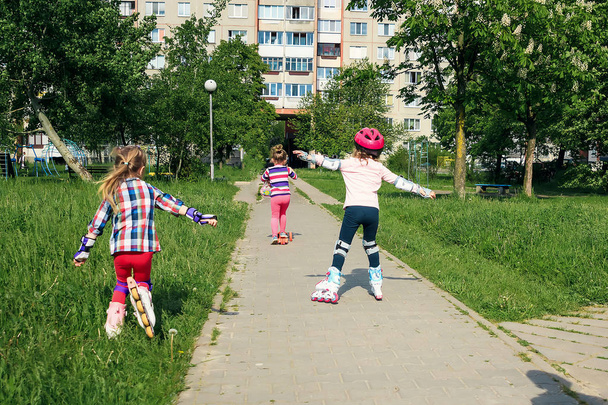 Girls learn to skate on the street. Children wear protective pads and a protective helmet for safe riding on rollers. Active sports activities for children - Foto, immagini